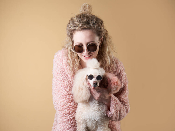 curly girl and poodle with glasses. A dog similar to its master. portrait in studio. modern, joke, beautiful, bright - Photo, Image