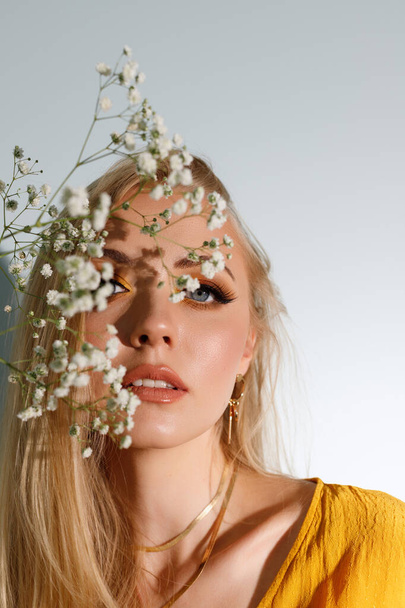 bright makeup in front of the model. the face is covered with flowers. fashion photo - Foto, afbeelding
