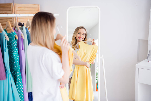 Photo portrait woman choosing dress in boutique fitting room looking at mirror reflection - 写真・画像