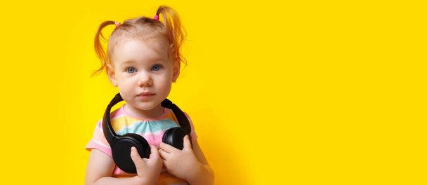 мила біла дитина з бездротовими навушниками, маленька дівчинка дивиться на камеру над жовтим тлом, панорамне планування з простором для тексту
 - Фото, зображення