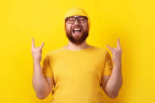 pozitivní člověk dělá rock n roll gesto přes žluté pozadí, lidé a tělo jazyk koncept - Fotografie, Obrázek
