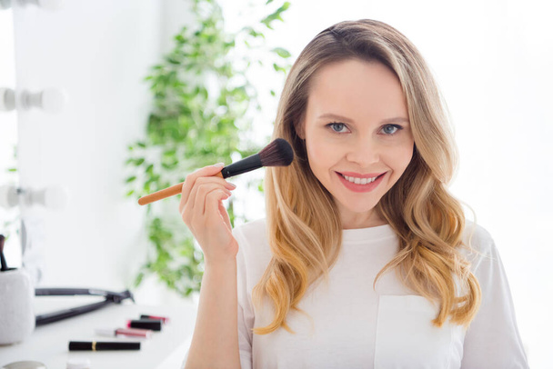 Photo portrait young woman in white clothes doing make up applying highlighter with brush - Foto, afbeelding