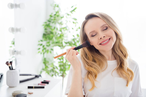 Portrait of attractive cheerful dreamy girl applying bb cream domestic makeup procedure at light white home indoors - Photo, Image