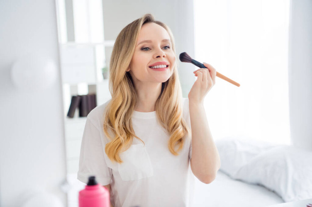 Photo portrait young woman in white clothes applying powder with brush near mirror - Foto, imagen