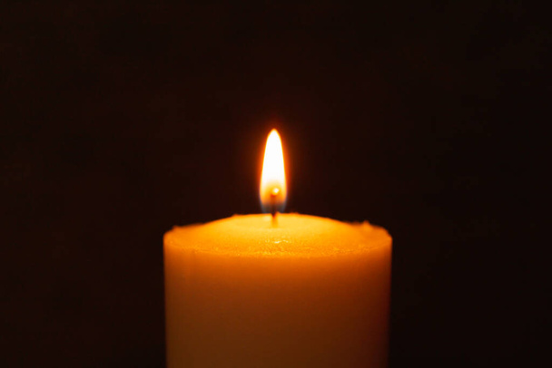 Eine einzige Kerze brennt hell im schwarzen Hintergrund. Geistliche Kerze gelbe Flamme. Kerzenflamme in der Dunkelheit. - Foto, Bild