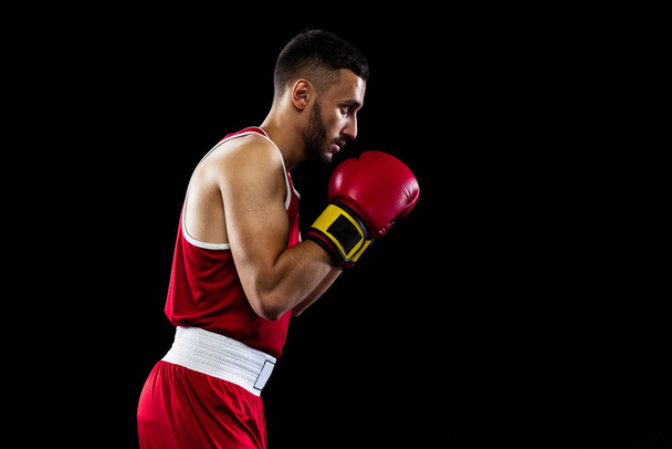 Egy vörös egyenruhás profi bokszoló portréja fekete háttérrel elszigetelve. Bajnoki felkészülés. Egészség, sport, mozgás. Reklámhely másolása. - Fotó, kép
