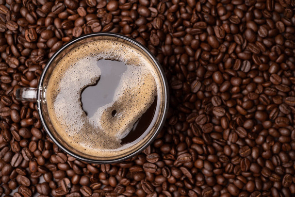 Het bovenaanzicht van een koffiekop en een groep zwarte koffiebonen is de achtergrond. Sterke zwarte espresso, Ondergronden van koffie achtergrond, textuur - Foto, afbeelding