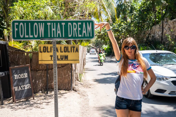 Beautiful female tourist showing motivational sign at roadside - Foto, afbeelding