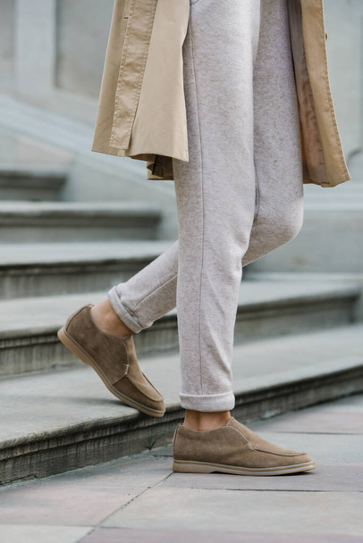 Portrait of fashionable women in beige pants and trench coat posing on the stone stairs - Foto, afbeelding