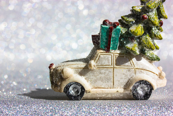 Λευκό αυτοκίνητο φορτηγό παιχνίδι με πράσινο χριστουγεννιάτικο πεύκο στην οροφή βόλτες σε ένα ασημί λαμπερό φόντο. Minimalistic ευτυχισμένη παραμονή Πρωτοχρονιάς φόντο. Ευχετήρια κάρτα, αντίγραφο χώρου. Μπλε παράδοση κουτί δώρου. - Φωτογραφία, εικόνα