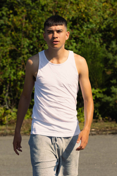 An 18 year old teen boy in a sleeveless top on a late summer's day - 写真・画像