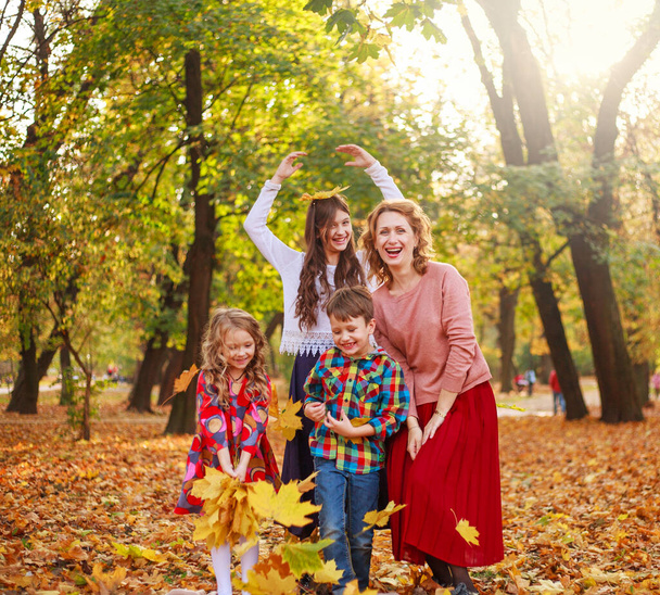 Family with three children actively having fun in the autumn park with fallen yellow foliage, seasonal holiday weekend - Φωτογραφία, εικόνα
