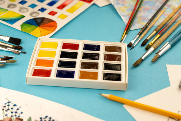 Eine Schachtel Aquarelle mit Pinseln. Zeichnung, Hintergrund. Verpackung von bunten neuen Farben auf dem Tisch. Pinsel und Farbe. Zeichnen und Basteln - Foto, Bild