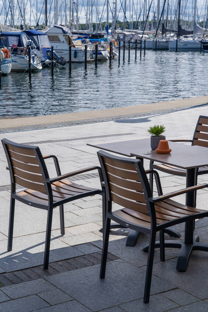 Empty table and chairs in front of a restaurant in the harbor of Heiligenhafen, Germany, in the background boats - 写真・画像