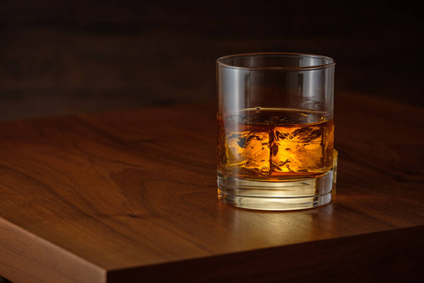 A glass of luxurious whiskey with ice cubes on wooden table - Foto, Imagem