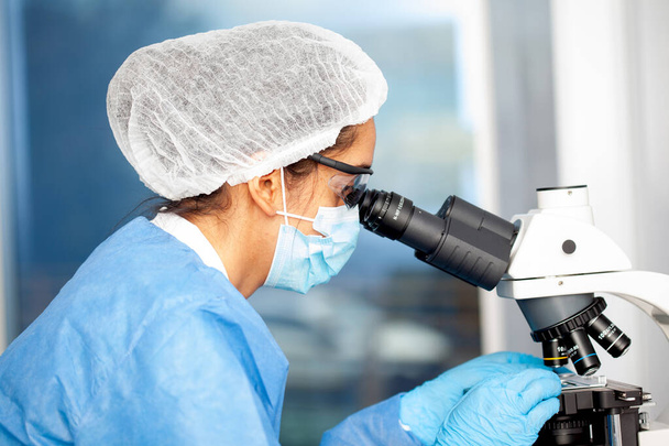 Νεαρή γυναίκα επιστήμονας που εξετάζει δείγματα κάτω από το μικροσκόπιο - Φωτογραφία, εικόνα