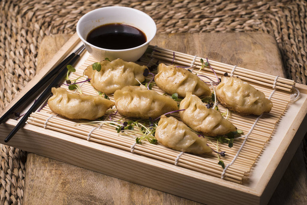 Japanese dumplings or gyoza served with soy sauce on a sushi mat on a board - 写真・画像