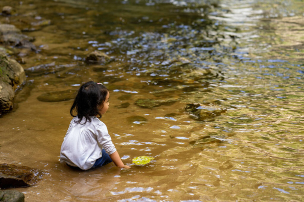 An adorable toddler sitting in the river in a park in the daylight in Thailand - Foto, Imagen