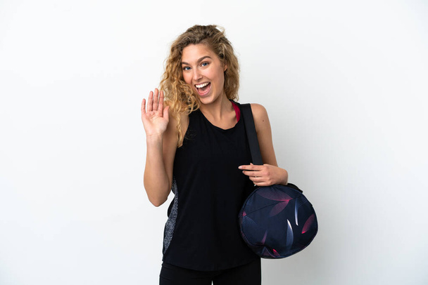 Young sport woman with sport bag isolated on white background saluting with hand with happy expression - Zdjęcie, obraz