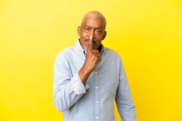 Cuban Senior aislado sobre fondo amarillo mostrando un gesto de silencio metiendo el dedo en la boca - Foto, Imagen