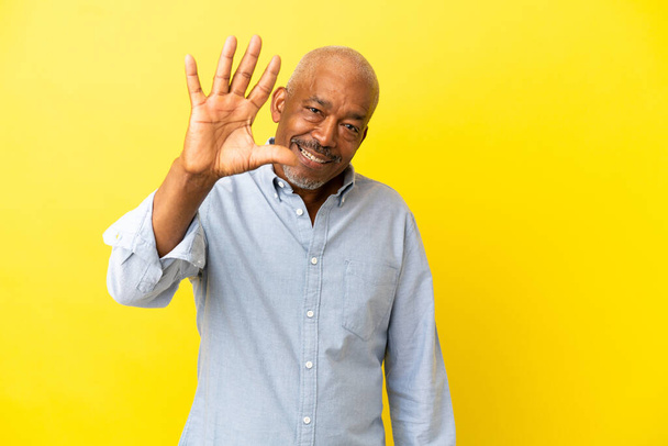Kubanischer Senior isoliert auf gelbem Hintergrund und zählt mit den Fingern fünf - Foto, Bild