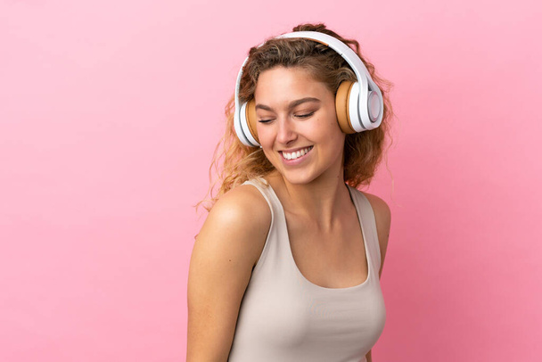 Young blonde woman isolated on pink background listening music - Photo, Image