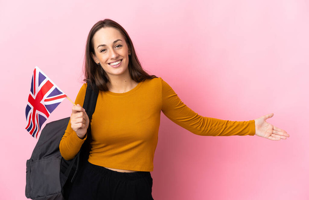 Joven mujer hispana sosteniendo una bandera del Reino Unido extendiendo las manos a un lado por invitar a venir - Foto, imagen