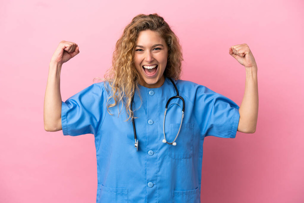 Junge Chirurgin Ärztin isoliert auf rosa Hintergrund tun starke Geste - Foto, Bild