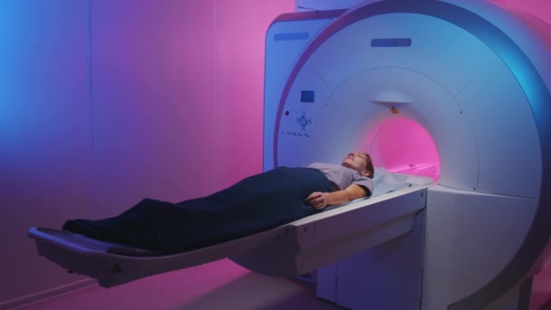 Prise de vue Slowmo d'une jeune femme ayant subi une IRM couchée sur une table de scanner dans une salle de radiologie avec éclairage bleu et violet - Séquence, vidéo