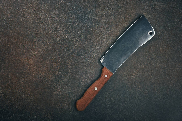 Cierre una cuchilla de carne de metal carnicero con mango de madera en la superficie de la mesa de la cocina grunge, vista superior elevada, directamente arriba - Foto, imagen