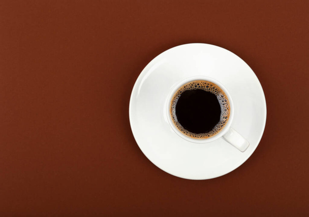 Cierre una taza blanca llena de café negro en platillo sobre el fondo de papel marrón, vista superior elevada, directamente arriba - Foto, Imagen