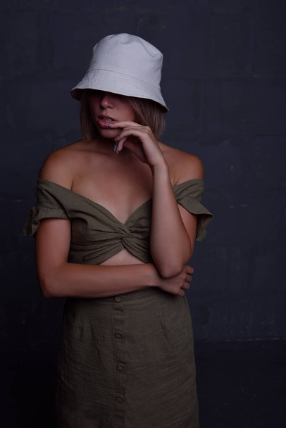 A young sexy woman in a dress and a panama hat covering her eyes. Studio photo on a dark background - Zdjęcie, obraz