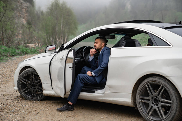 attractive man in business suit sits behind wheel of car with door open. - Photo, image