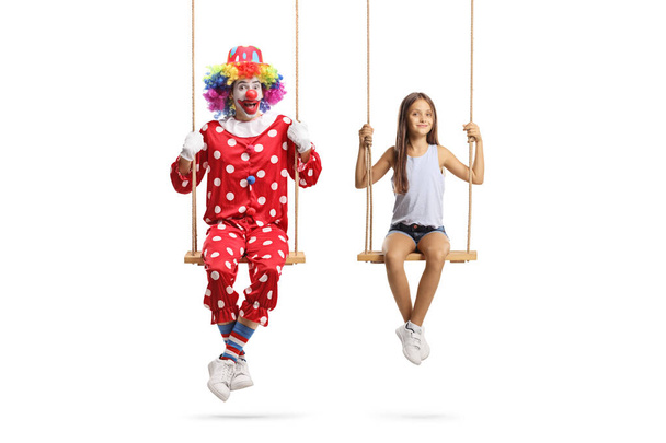 Girl and a clown sitting on wooden swings and looking at camera isolated on white background - Foto, Bild