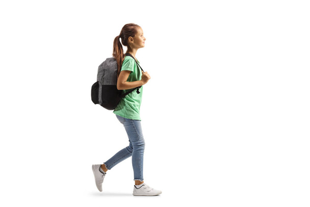 Full length profile shot of a girl carrying a backpack and walking isolated on white background - Fotó, kép