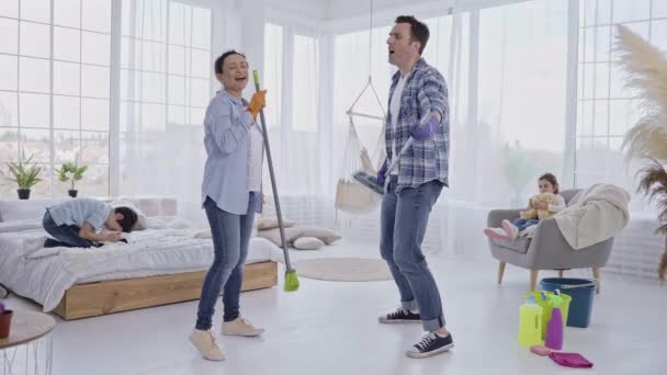 Padres alegres bailando con dispositivos de limpieza - Metraje, vídeo