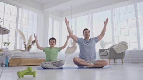 Uomo con figlio che fa yoga seduto sul tappeto a casa - Filmati, video