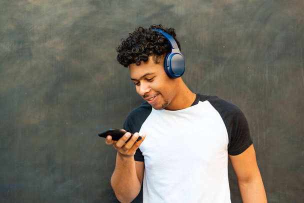 Afro latin young man listening to music against a wall - Фото, зображення
