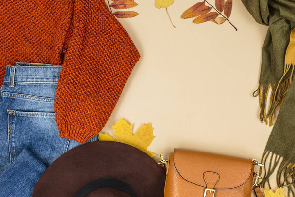 Skórzana torba pomarańczowa, sweter z dzianiny, szalik, jesienne liście na beżowym brązowym tle. Modne jesienne akcesoria. Przytulny strój - Zdjęcie, obraz