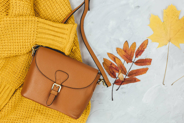 Bolso para mujer de cuero naranja, suéter de punto, hojas de otoño sobre fondo gris. Accesorios de otoño de moda. Traje acogedor - Foto, imagen