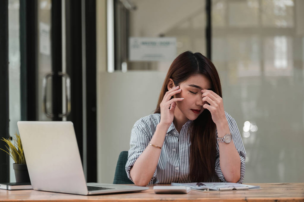 Mujer joven estresada sentada en el escritorio trabajando desde la oficina en el hogar, dolor de cabeza de mujer de negocios mientras tiene un problema en el trabajo en la oficina - Foto, imagen