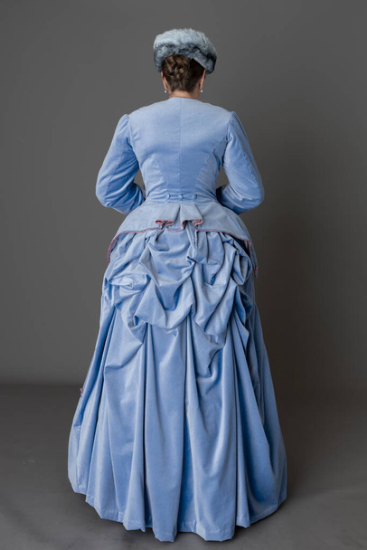 A Victorian woman wearing a pale blue velvet bustle ensemble with a fur hat and muff - Фото, изображение