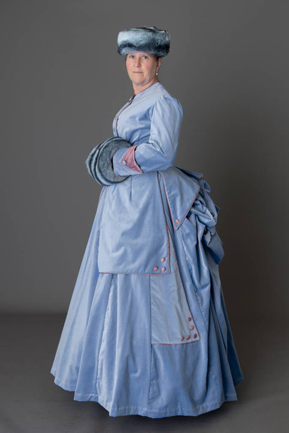 Viktorya Dönemi 'nden soluk mavi kadife bir kadife elbise giyen kürk şapkalı ve kuklalı bir kadın. - Fotoğraf, Görsel