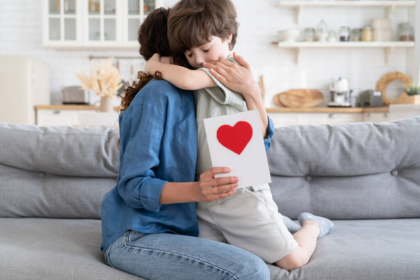 Kleuterjongen knuffelende moeder heeft een wenskaart. Klein kind gefeliciteerd moeder aanwezig ansichtkaart - Foto, afbeelding