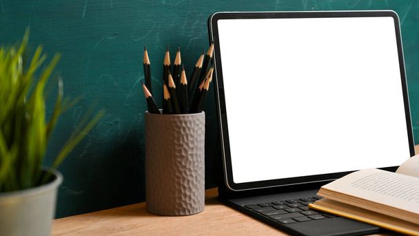 Vista lateral de la tableta digital maqueta de pantalla blanca con libro abierto, lápices sobre fondo de pizarra verde. volver al concepto escolar - Foto, imagen