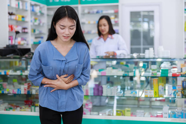 female patient stomach ache in pharmacy and doctor with shelf medicine background in Thailand - Φωτογραφία, εικόνα