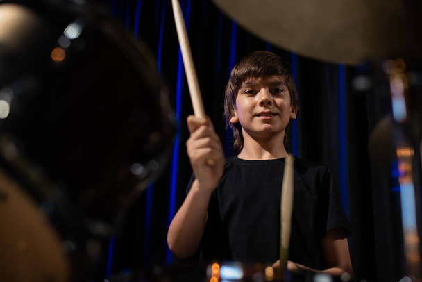 The boy learns to play the drums in the studio on a black background. Music school student - Fotoğraf, Görsel