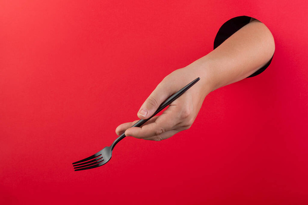 A female hand holds black cutlery on a red background. Template for design. Space for text. - Фото, изображение