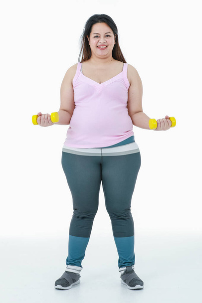 Portrait isolated studio shot of Asian happy healthy strong big fat girl standing smiling lifting pink and yellow dumbbells with two arms in weight lose practice exercise in front white background. - Photo, Image