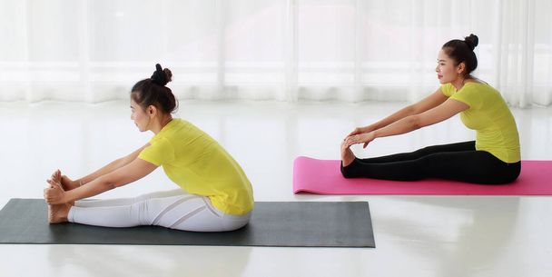 Mladá žena a trenérka jógy cvičící Paschimottanasana pózují ve studiu jógy. Zdravý životní styl a fitness koncept. - Fotografie, Obrázek